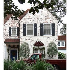 a red truck parked in front of a white brick house with black shuttered windows