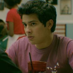 a young man sitting at a table with a drink in front of him and two other people behind him