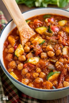 a white bowl filled with beans and zucchini on top of a wooden table