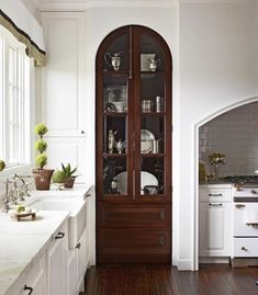 a kitchen with white cabinets and wood flooring next to a large glass doored cabinet