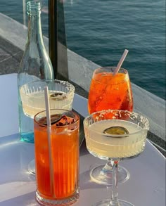 two drinks sitting on top of a table next to each other near the ocean and water