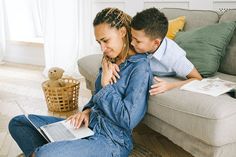 a woman sitting on top of a couch next to a boy using a laptop computer