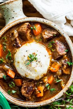 a bowl filled with meat and carrots on top of a wooden table next to a spoon