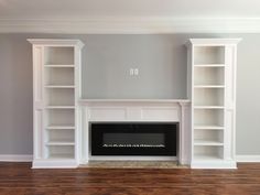 an empty living room with white bookcases and a fireplace