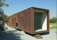 an outhouse sits in the middle of a gravel area with trees and grass around it