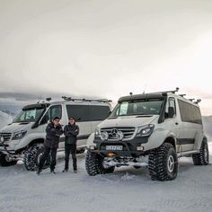 two men standing next to four mercedes benz vans in the snow