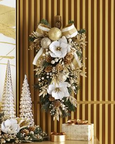 a christmas wreath with white flowers and gold decorations on a table next to a gift box