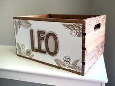 a wooden box sitting on top of a white table next to a planter with the word leo printed on it