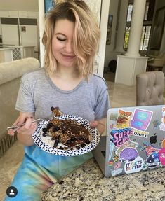 a woman sitting at a table with a plate of food in front of her laptop