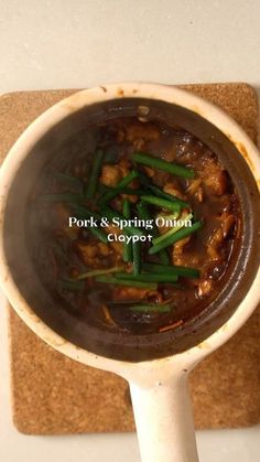 a pot filled with meat and green beans on top of a wooden spatula next to a cork board