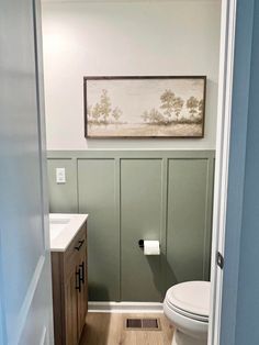 a white toilet sitting in a bathroom next to a wooden cabinet and sink under a painting