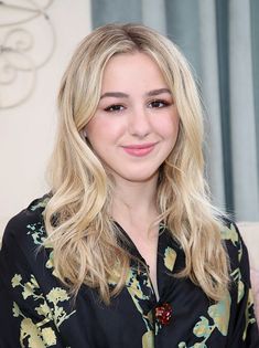 a woman with long blonde hair wearing a black and green shirt smiling at the camera