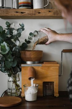 a person pouring something into a cup on top of a wooden table next to a potted plant