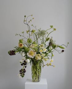 a vase filled with lots of flowers on top of a white table next to a wall