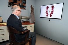 a man sitting in a chair looking at a large screen with blood on it's surface