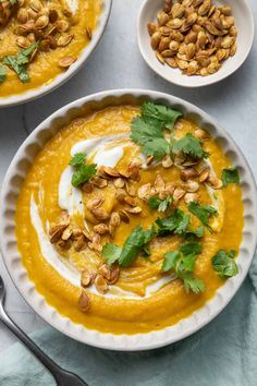 two bowls filled with carrot soup and topped with nuts