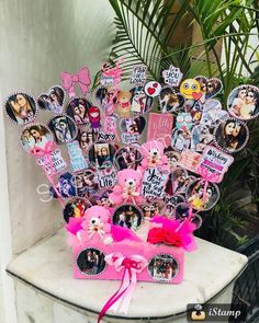 a vase filled with lots of pictures and pink ribbon on top of a table next to a potted plant