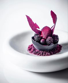 a white plate topped with raspberries and blackberries covered in purple powdered sugar