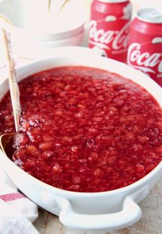 a white bowl filled with red liquid next to coca cola cans