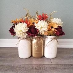 three mason jars with flowers in them sitting on the floor