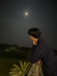 a man standing on top of a balcony next to a lush green field at night