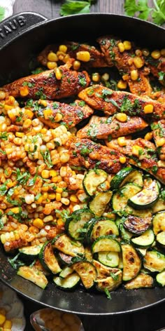 a skillet filled with chicken, zucchini and corn on the cob