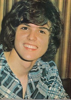 an old photo of a young man with long hair and plaid shirt smiling at the camera