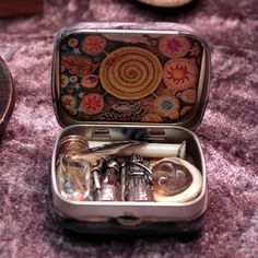 an open tin box with silverware inside on a purple tableclothed surface next to other items