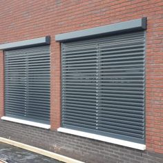 the side of a brick building with three windows and two roller shades on each window