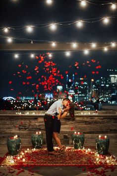 a man and woman kissing in front of candles on the ground with red flowers around them