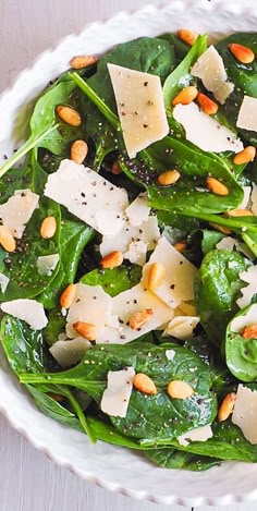 spinach salad with pine nuts and parmesan cheese in a white bowl on a table