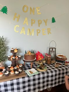 a table topped with cakes and cupcakes under a one happy camper banner