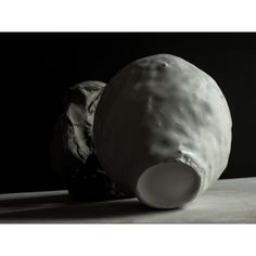 a white vase sitting on top of a table next to a black background and an object in the foreground