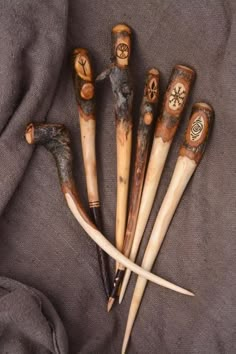 five wooden sticks with carved faces are arranged in a row on a gray fabric background