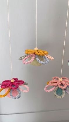 three crocheted flower mobiles hanging from strings in a room with gray walls