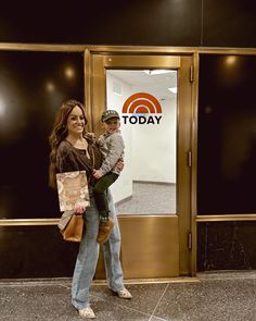 a woman holding a small child in front of a building with a today sign on it