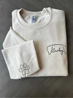 a white shirt with a dog's paw on it and a small embroidered t - shirt