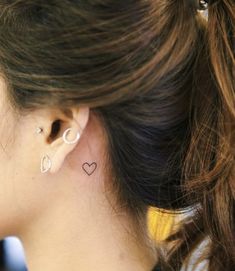 a woman wearing ear piercings with a heart tattoo on her left side of the ear