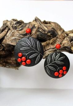 the earrings are decorated with red beads and black leaf designs on them, sitting on a piece of driftwood