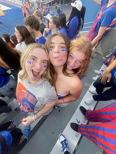 three girls with their faces painted in blue and orange are posing for the camera at a football game