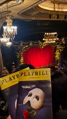 a person holding up a playbill book in front of a stage