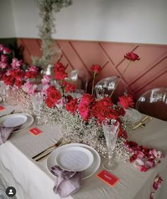 the table is set with red flowers and place settings for two people to sit at