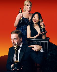 two women and one man holding their oscars in front of an orange background,