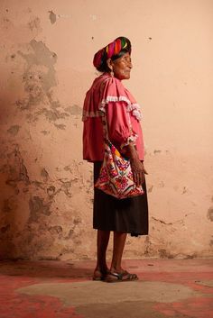 an old woman standing in front of a wall wearing a pink top and black skirt