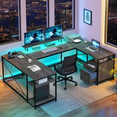 an office desk with two monitors, keyboard and mouse in front of large windows overlooking the city at night