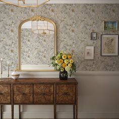 a vase with yellow flowers sitting on top of a wooden table next to a mirror