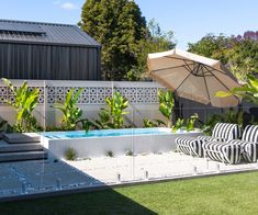 an outdoor pool with lounge chairs and umbrellas next to it in a backyard area