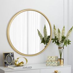 a white dresser topped with a mirror next to a vase filled with flowers and plants