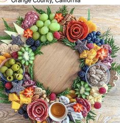 an arrangement of fruits and vegetables arranged in a wreath on a wooden table with a cup of coffee