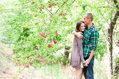 a man and woman standing in front of an apple tree with their arms around each other